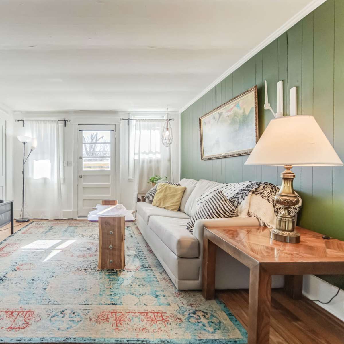 The living room features a sofa, a coffee table, a television, and large windows, with green accent walls and a decorative rug.