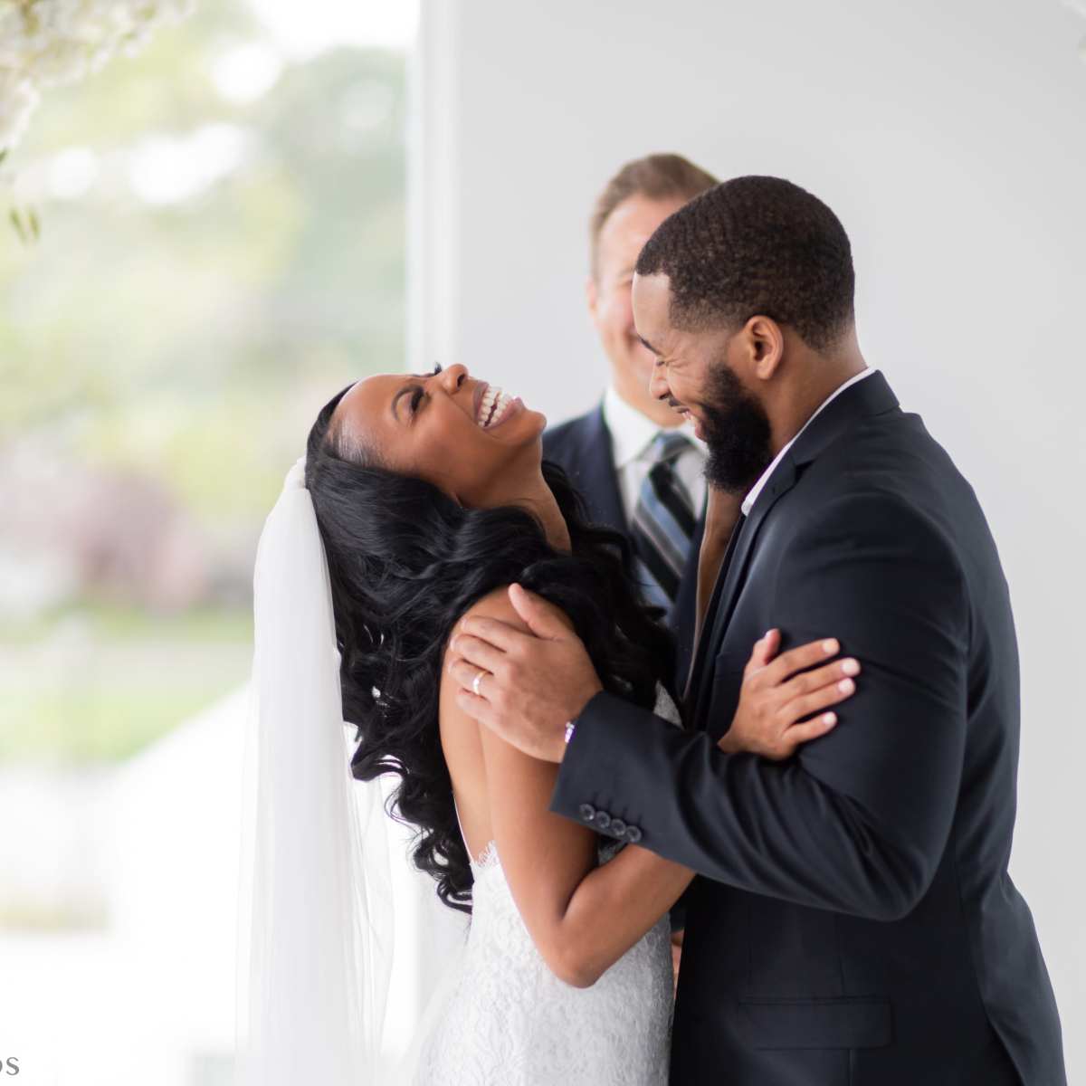 A couple smiles and embraces during their wedding ceremony, with a officiant standing behind them.