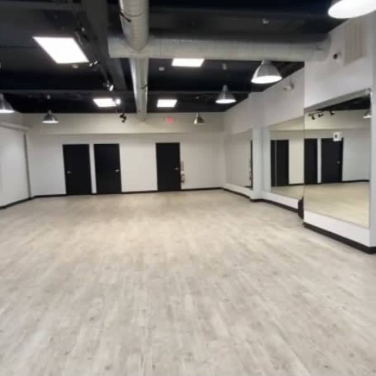 An empty room with light-colored wooden flooring, white walls, and large mirrors on one side.