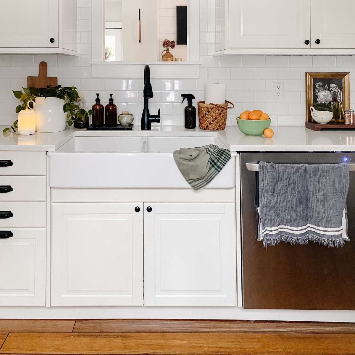 The kitchen features a farmhouse-style sink, white cabinetry, and a mirror framed with wood above the countertop.
