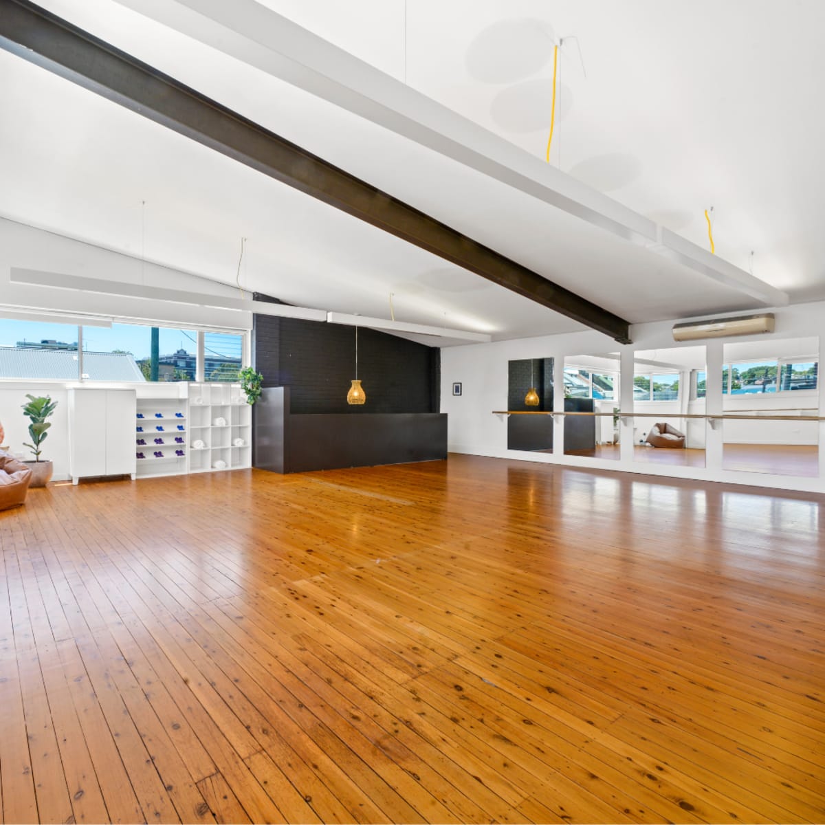 A spacious interior with wooden flooring, large windows, and a minimalistic design featuring a seating area and an island counter.
