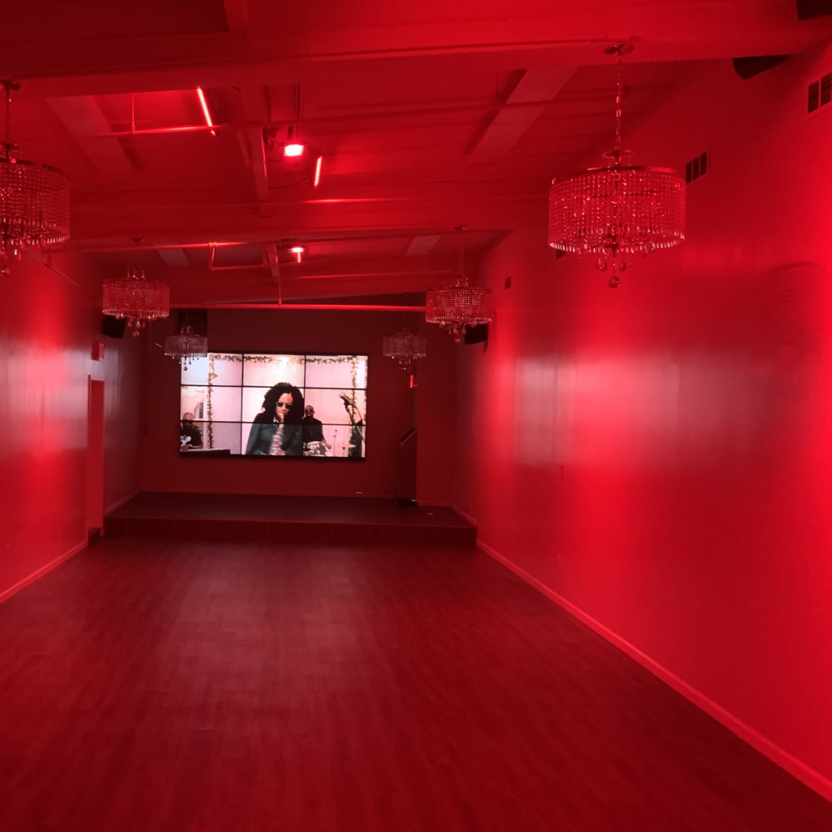 The room features red lighting, chandeliers, and a large screen displaying a video at the far end.