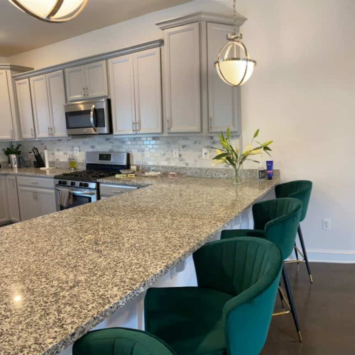 A modern open-concept living space with a kitchen featuring a granite countertop and bar seating, an entertainment area with a fireplace, and ample natural light from large windows.