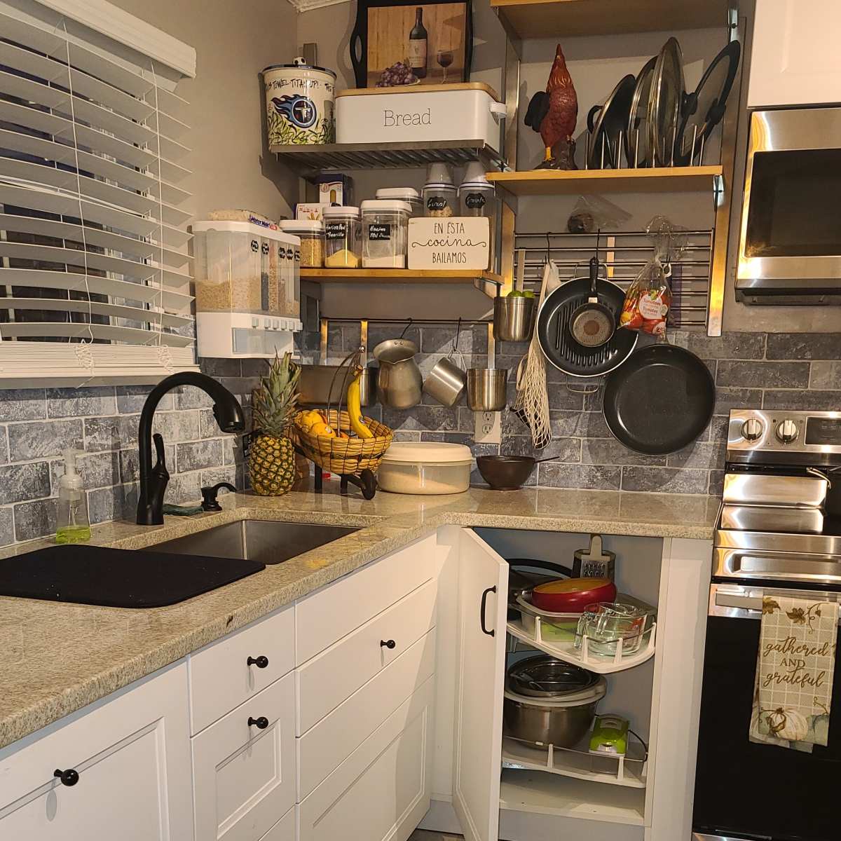 A modern kitchen with white cabinetry, open shelving holding utensils and food items, and a black sink with a countertop and appliances.