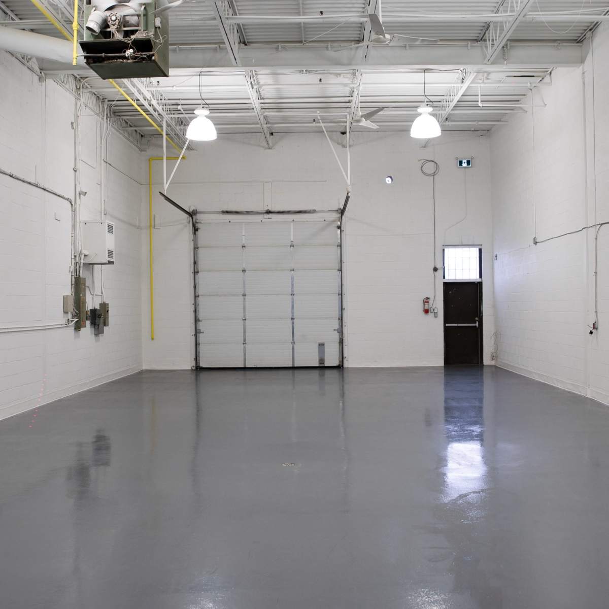 A vacant, well-lit industrial space with a smooth, polished concrete floor and a large overhead garage door.
