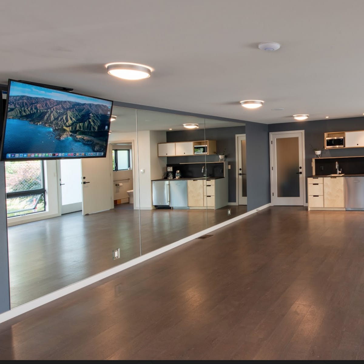 A spacious, modern room with a kitchen area and large mirrors on one wall.