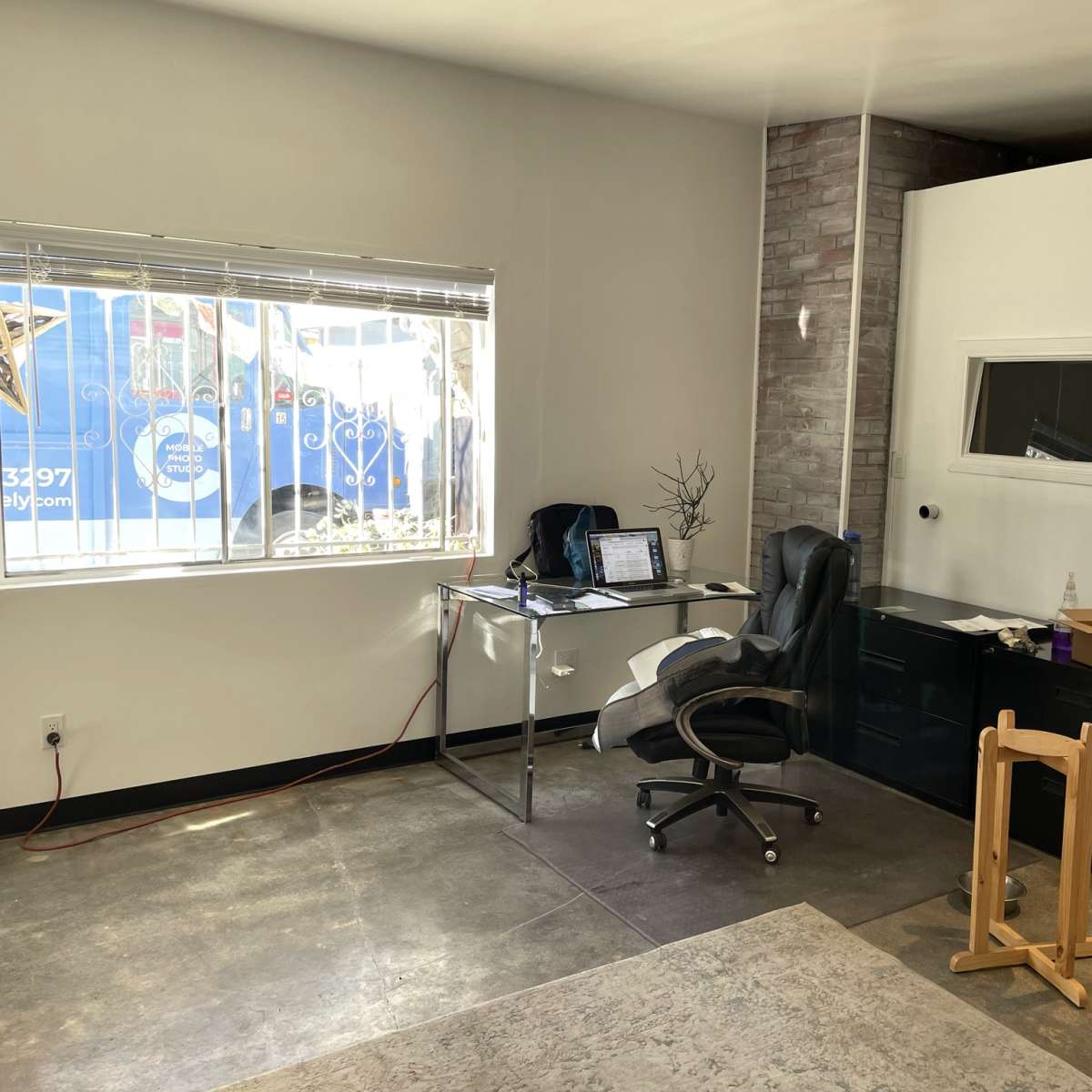 A modern office space with a desk, chair, and a large window revealing a partial view of a vehicle outside.