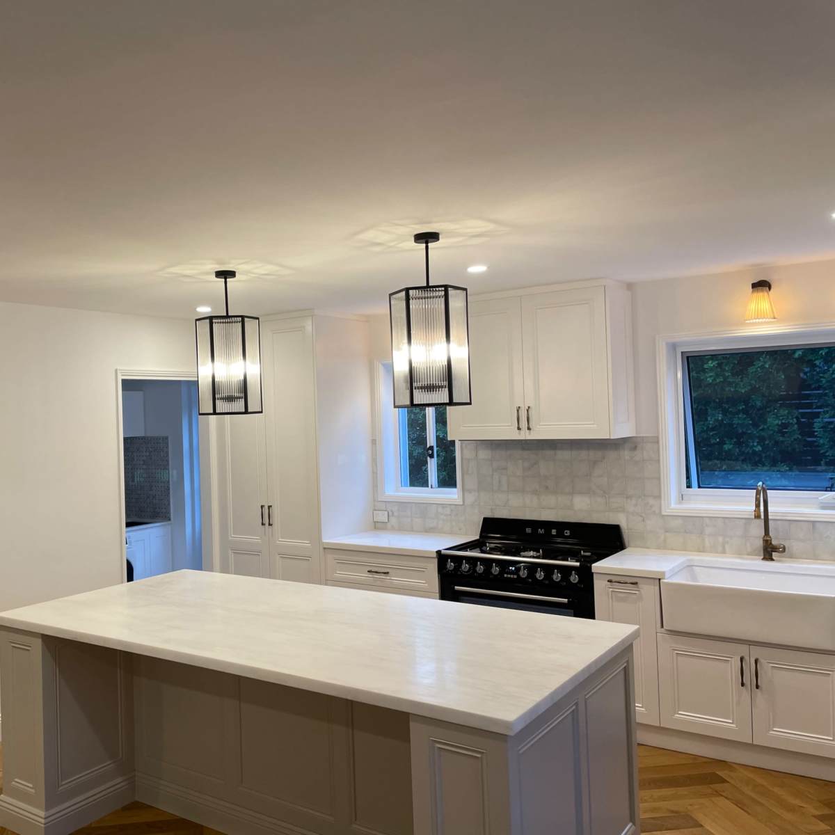 A modern kitchen featuring a central island, pendant lighting, white cabinets, and a large window above the sink.
