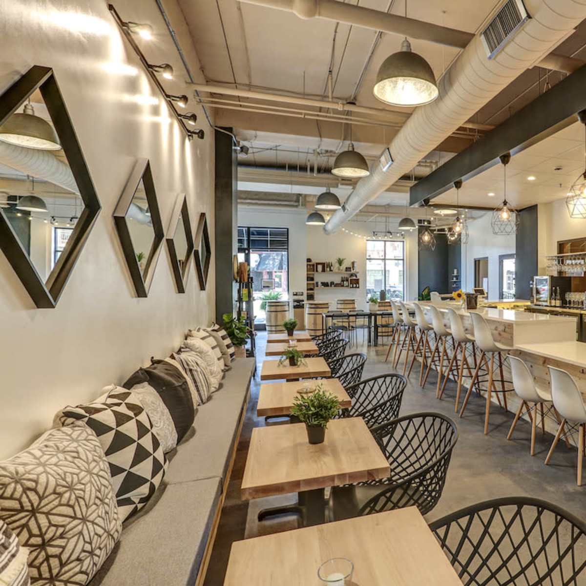 A modern café interior with a seating area featuring wooden tables, black chairs, and a long bar counter with stools.