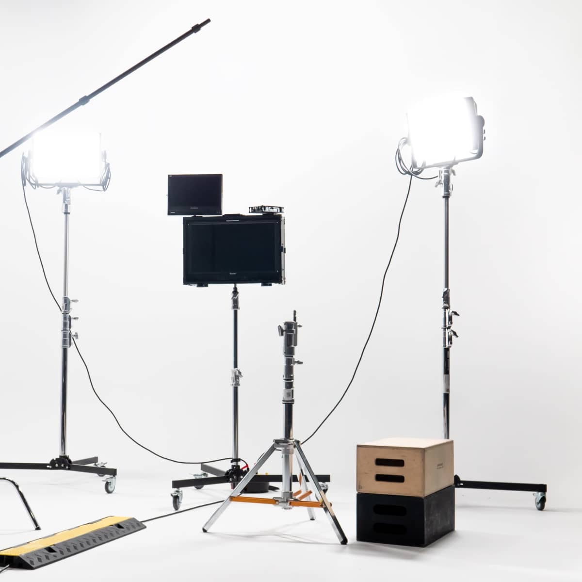 A photography setup with two lighting stands, a monitor on a tripod, and a few equipment boxes on a plain white background.