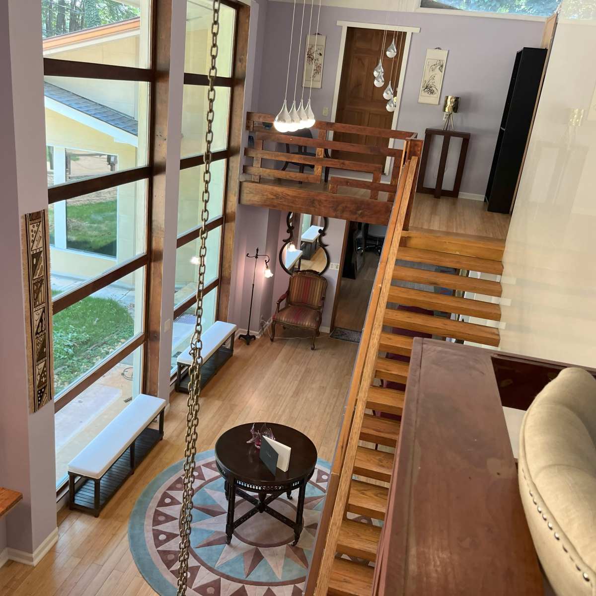 A modern interior space with large windows, a staircase, a round table, and seating areas under well-lit conditions.
