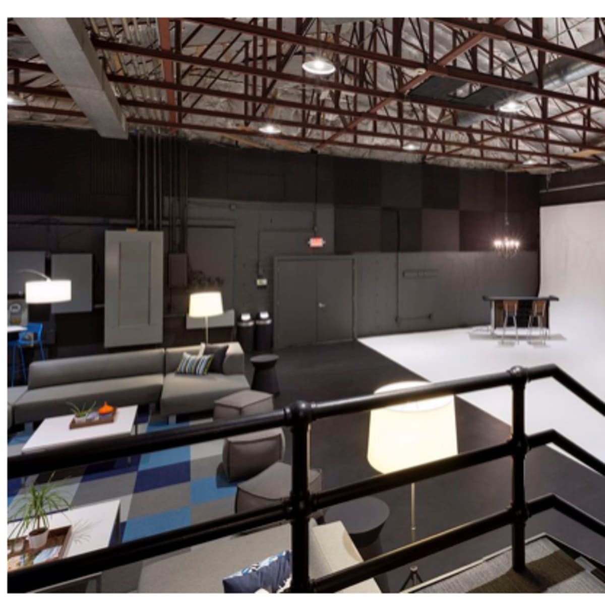 A spacious studio with a white backdrop, modern furniture, and exposed metal beams in the ceiling.