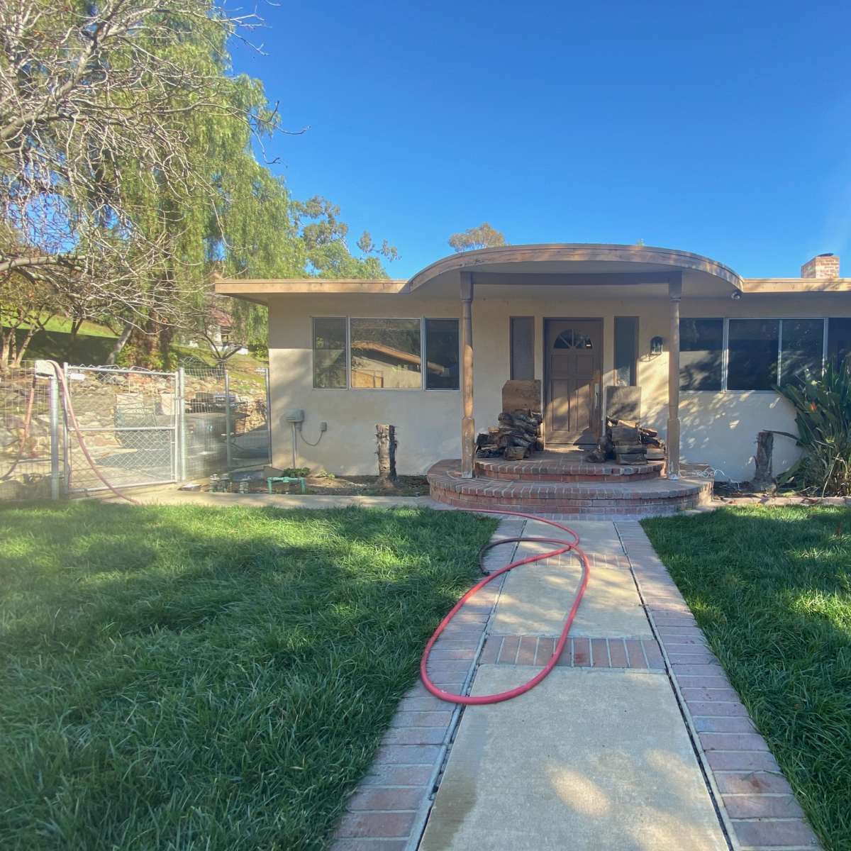 A single-story house with a front porch, a concrete walkway leading to the entrance, and a yard with grass and shrubs.