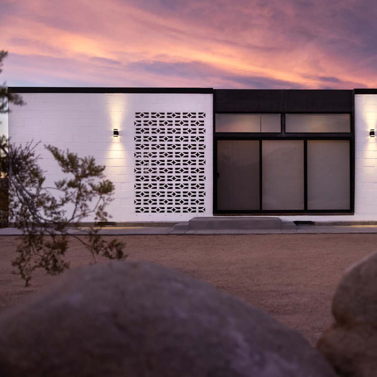 A modern white building features large windows and accent lights, set against a colorful sky at sunset.