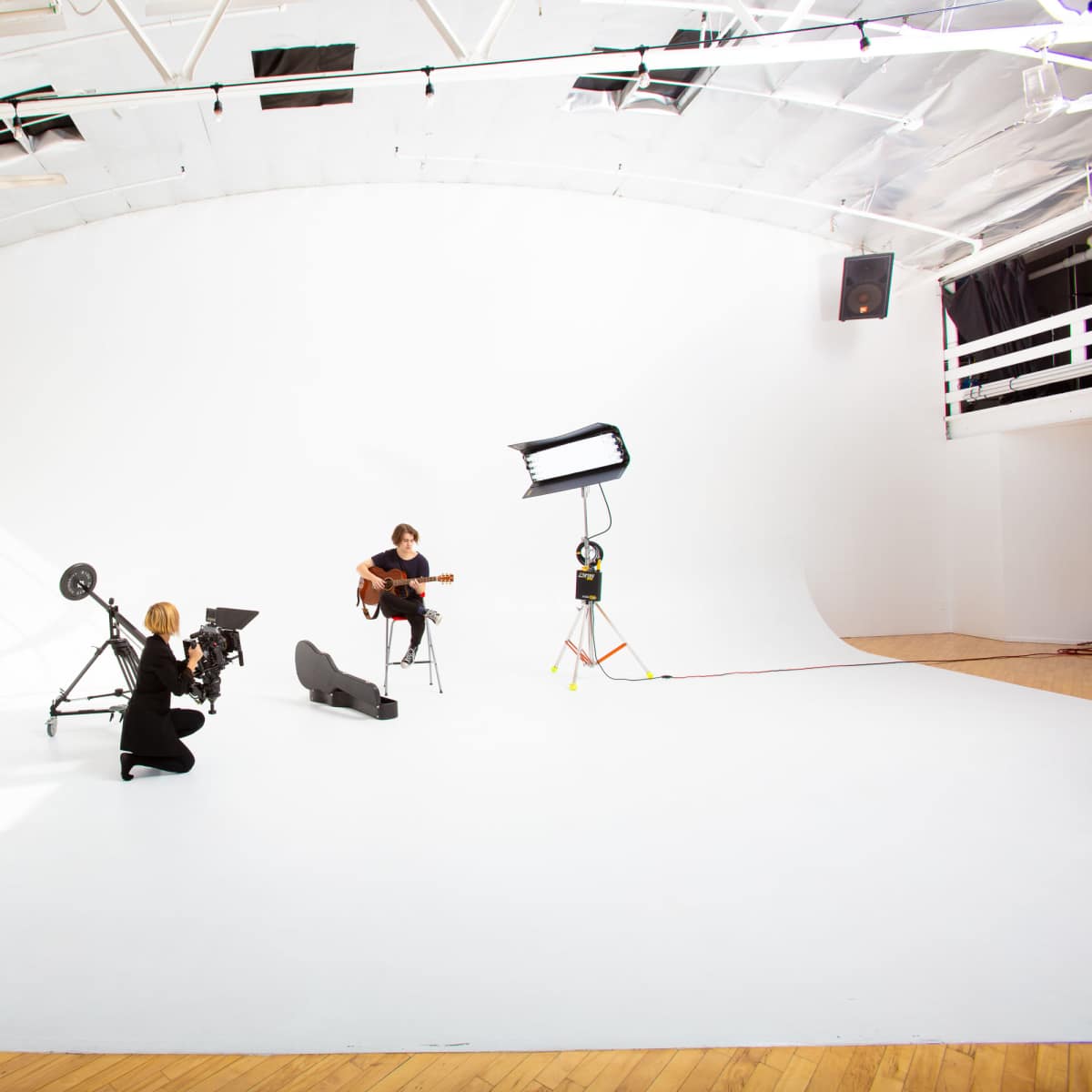 A photographer captures a musician playing guitar in a spacious, well-lit photo studio with a white backdrop.