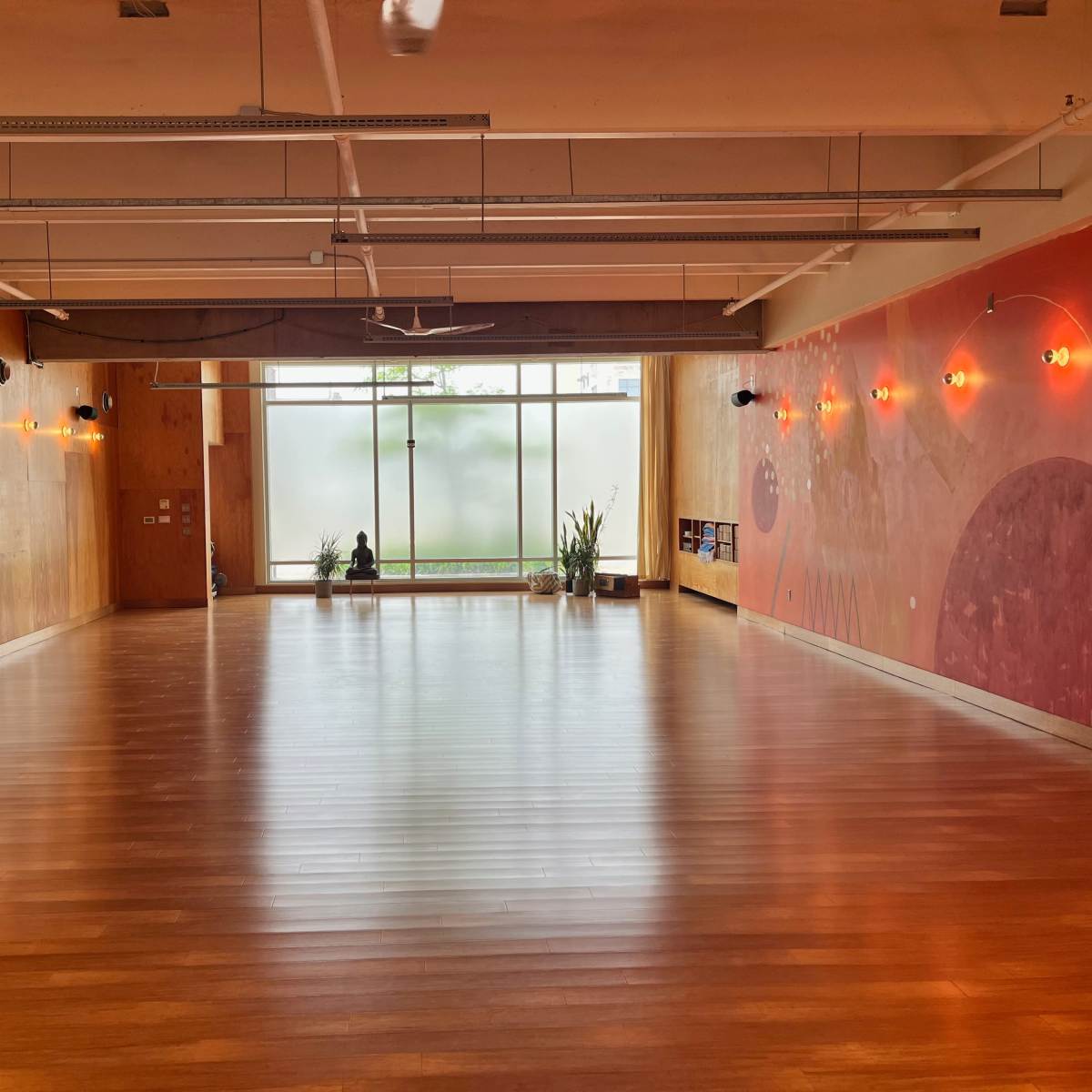 A spacious interior room with hardwood flooring, large windows allowing natural light, and decorative wall art.
