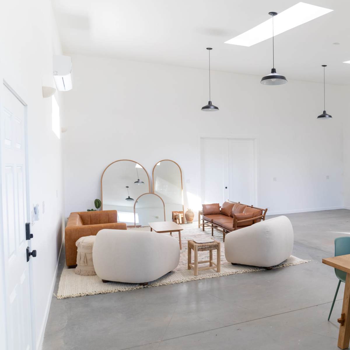A modern, spacious interior featuring a seating area with two sofas, two decorative mirrors, and a large dining table with green chairs.
