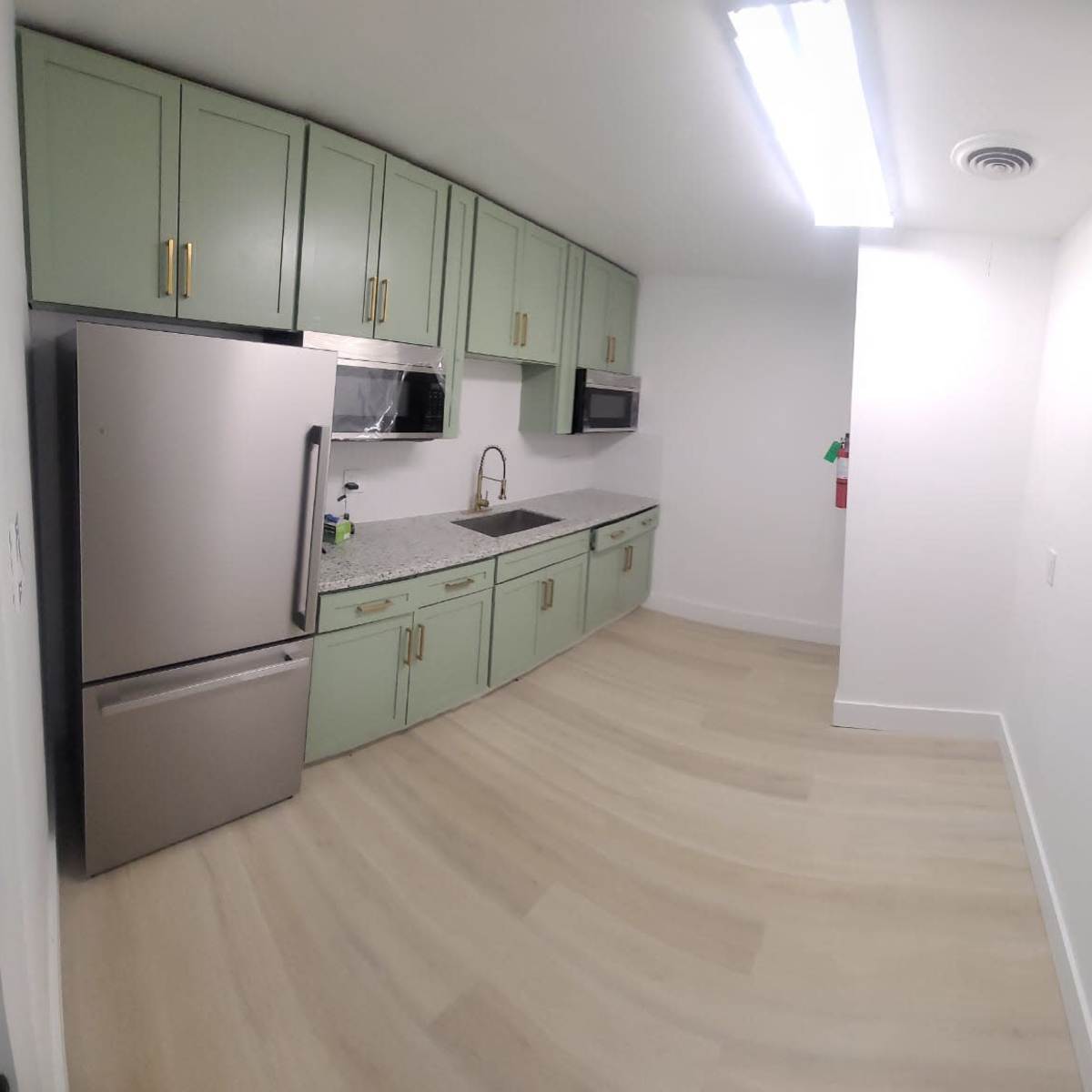 A modern kitchen with light green cabinets, stainless steel appliances, and a countertop with a sink.