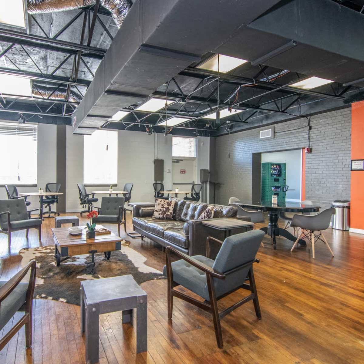 A spacious modern office or co-working area with gray walls, wooden floors, and various seating arrangements including tables and chairs.