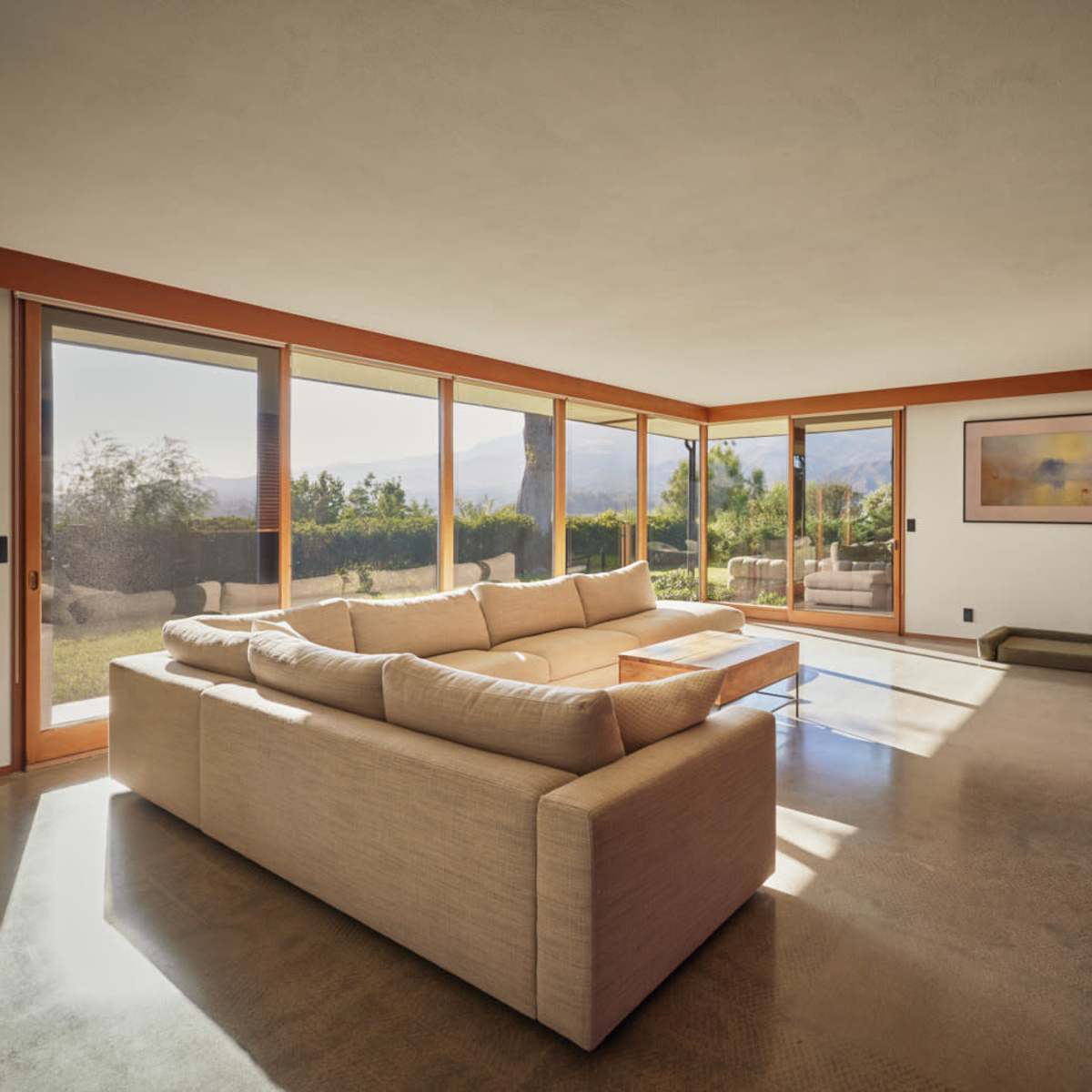 A modern living room with large windows, a sectional sofa, a brick wall, and a view of an outdoor landscape.