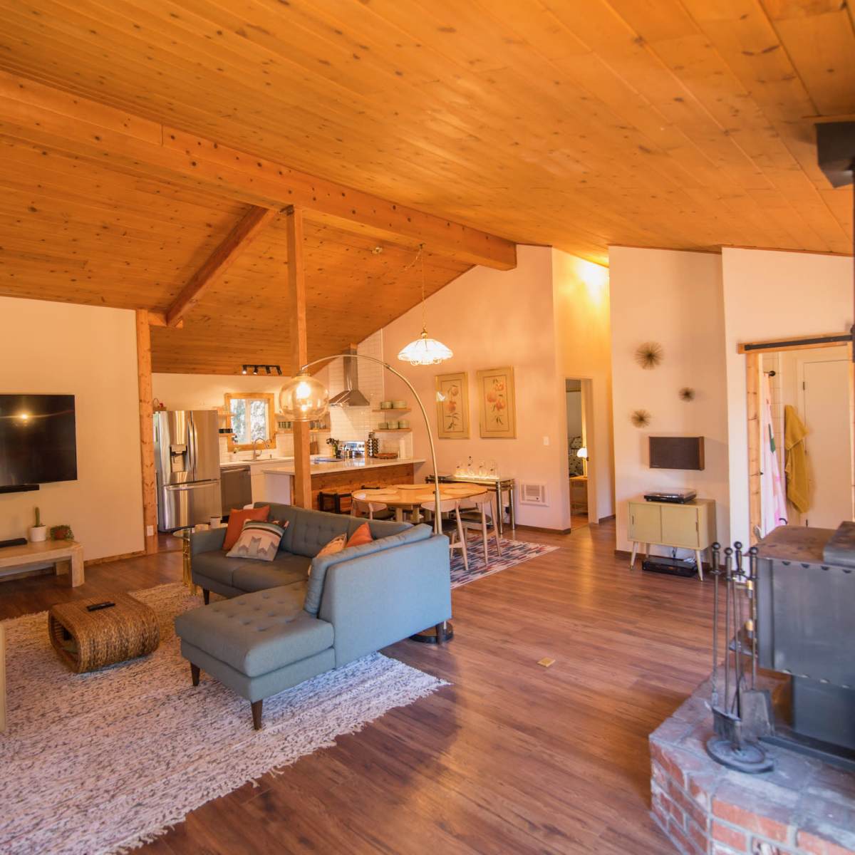 An open-concept living area with a wooden ceiling, two seating arrangements, a television, and a dining area in the background.