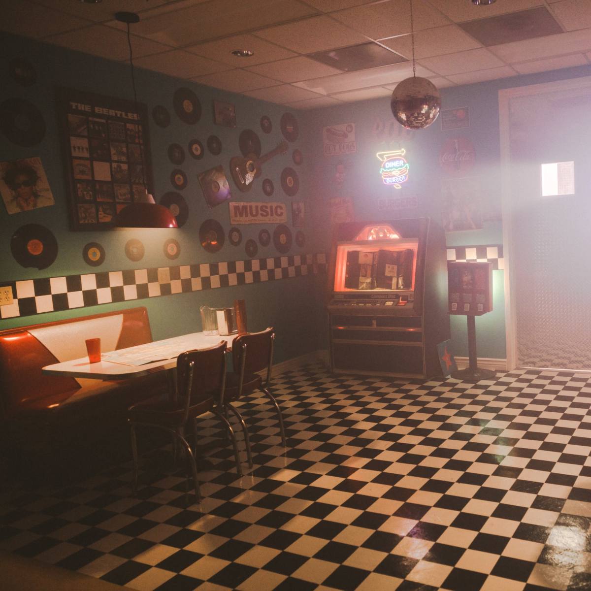 A retro diner features checkered flooring, red booths, a jukebox, and vinyl records decorating the walls, all shrouded in a misty ambiance.