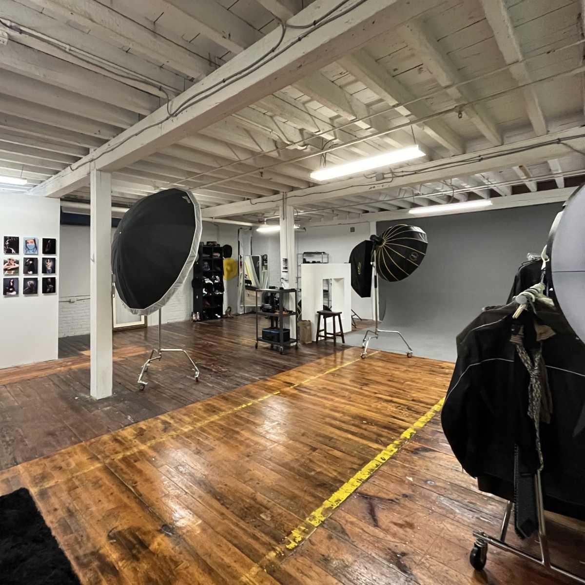 A spacious photography studio featuring a gallery wall of portraits, large softboxes mounted on stands, and wooden flooring.