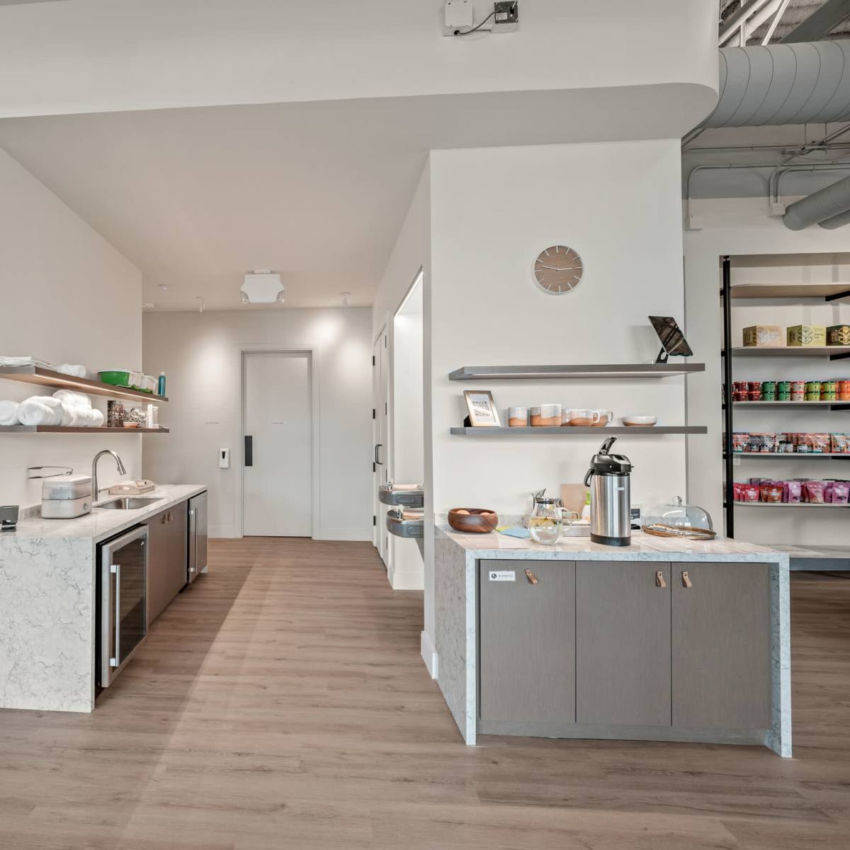 A modern interior features a kitchen area with a marble countertop and organized shelves displaying storage containers and products.