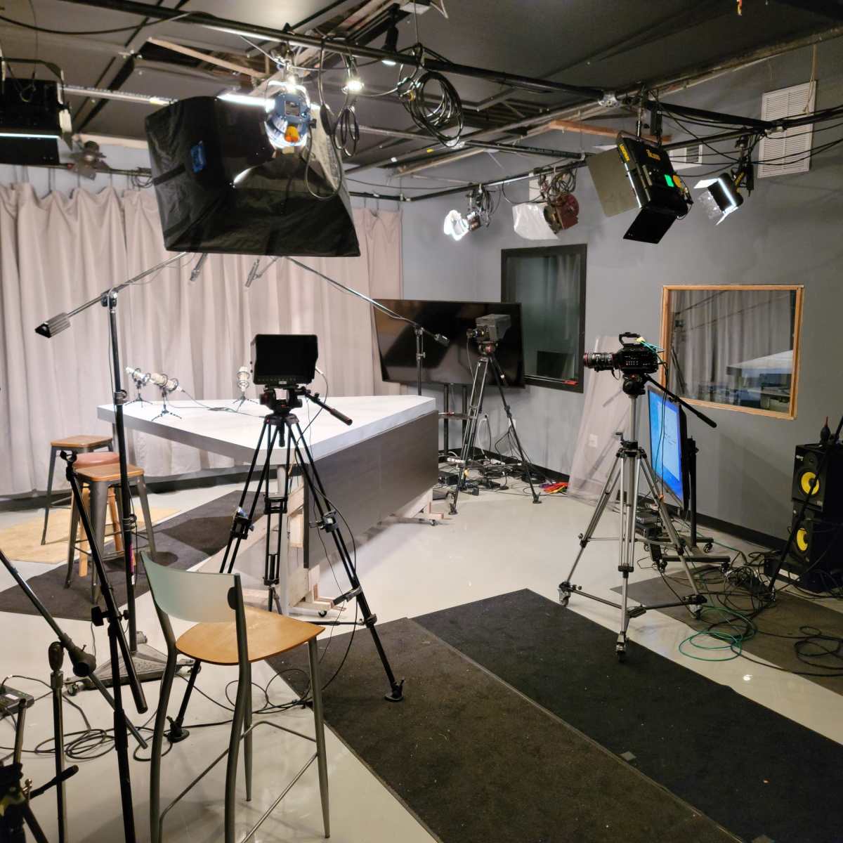 A television studio setup with cameras, lighting equipment, a central table, and a backdrop of curtains.