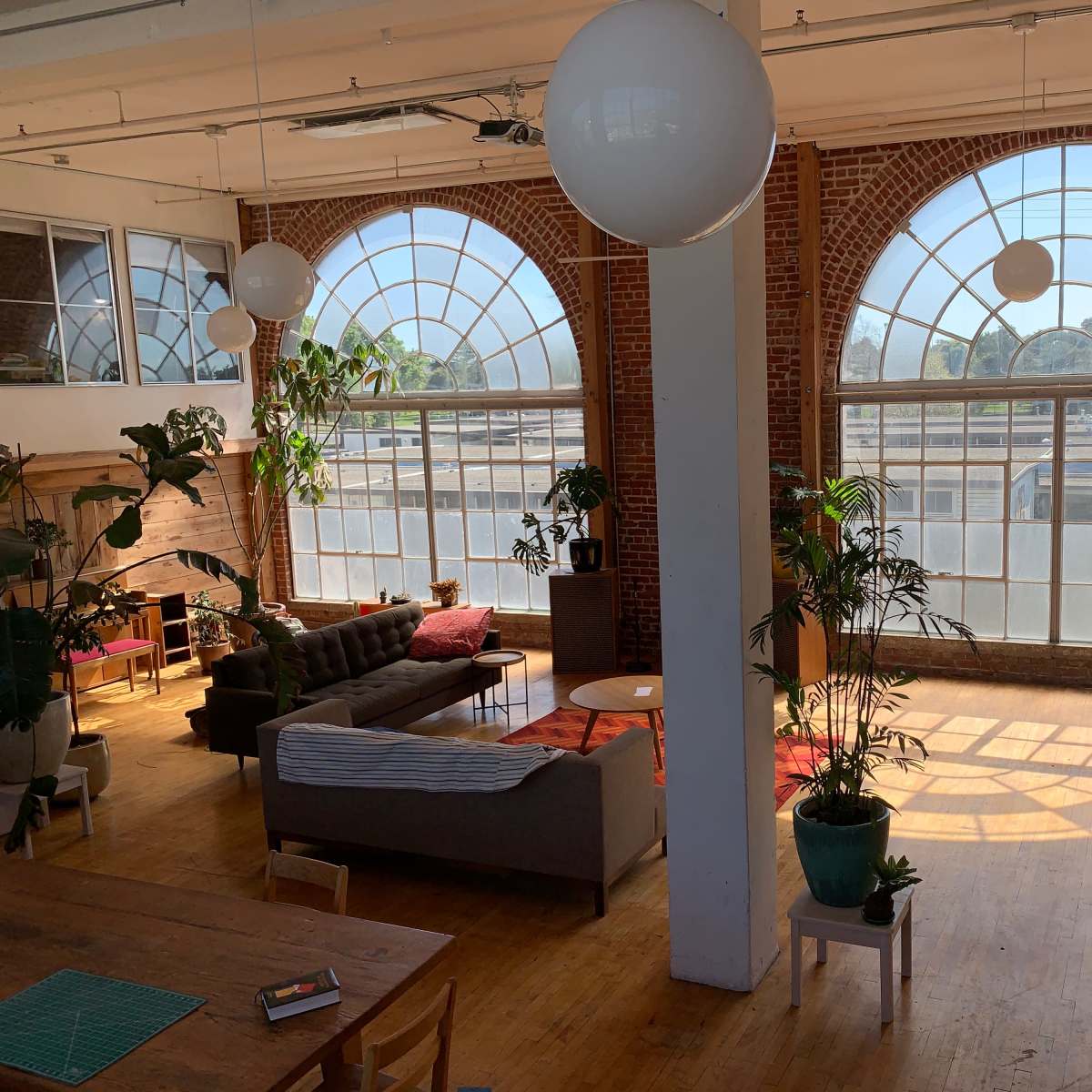 A spacious loft with large arched windows, brick walls, and a seating area featuring a couch, plants, and a coffee table.