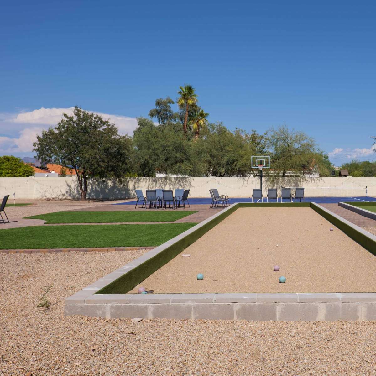 A bocce ball court surrounded by seating areas and greenery under a clear blue sky.
