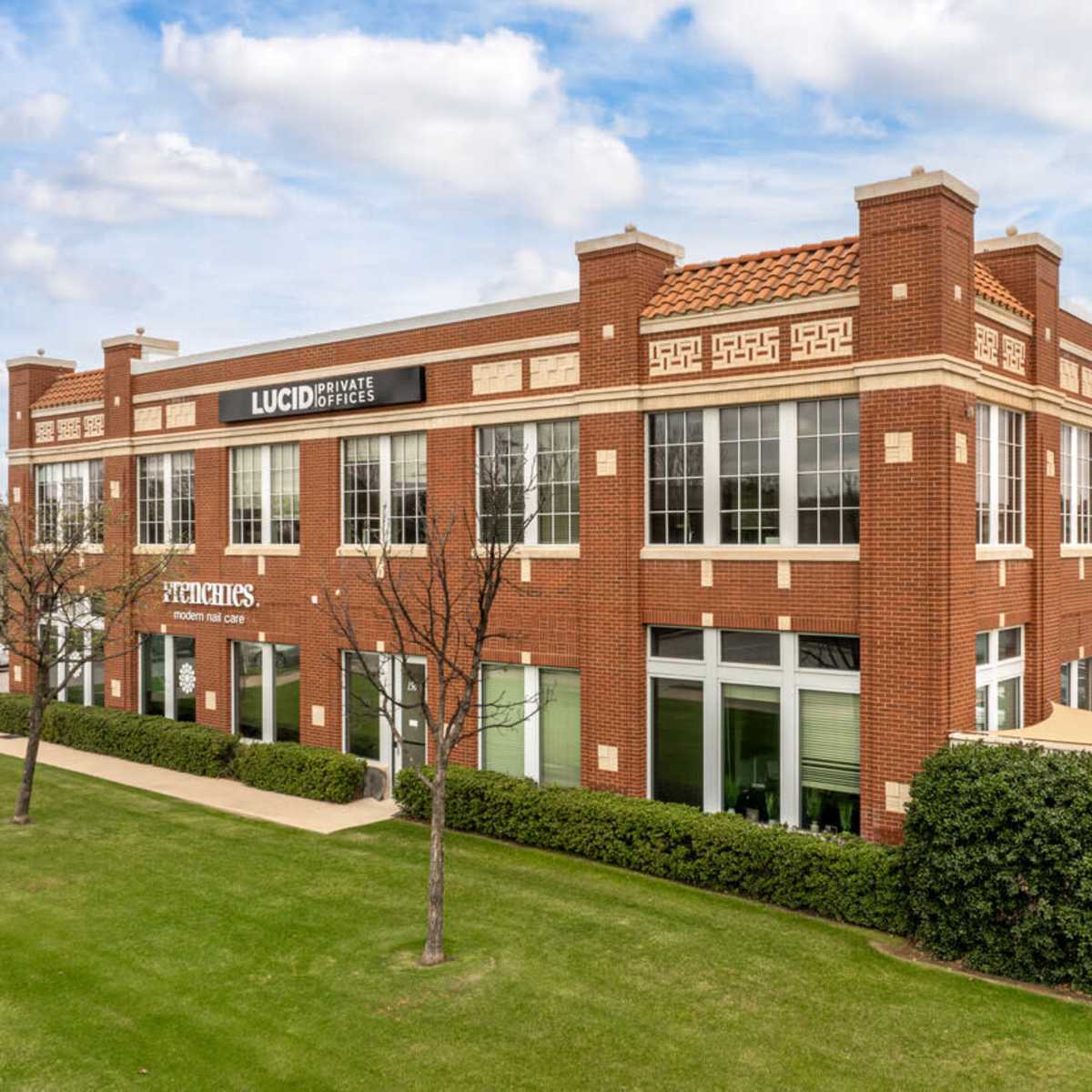 A modern two-story brick building with large windows and a landscaped lawn in front.
