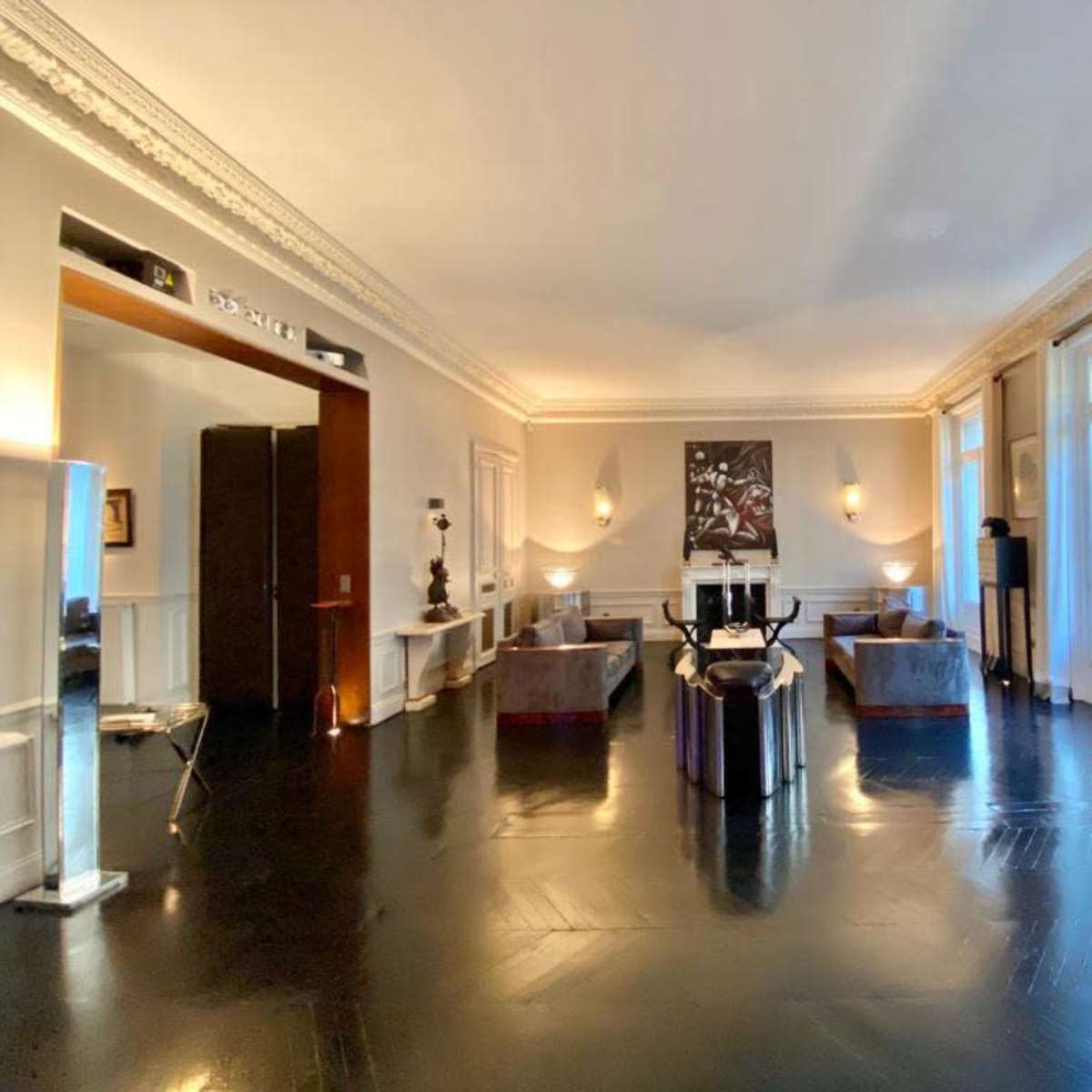A spacious living room with dark wooden floors, large windows, and contemporary furniture arranged around a central seating area.