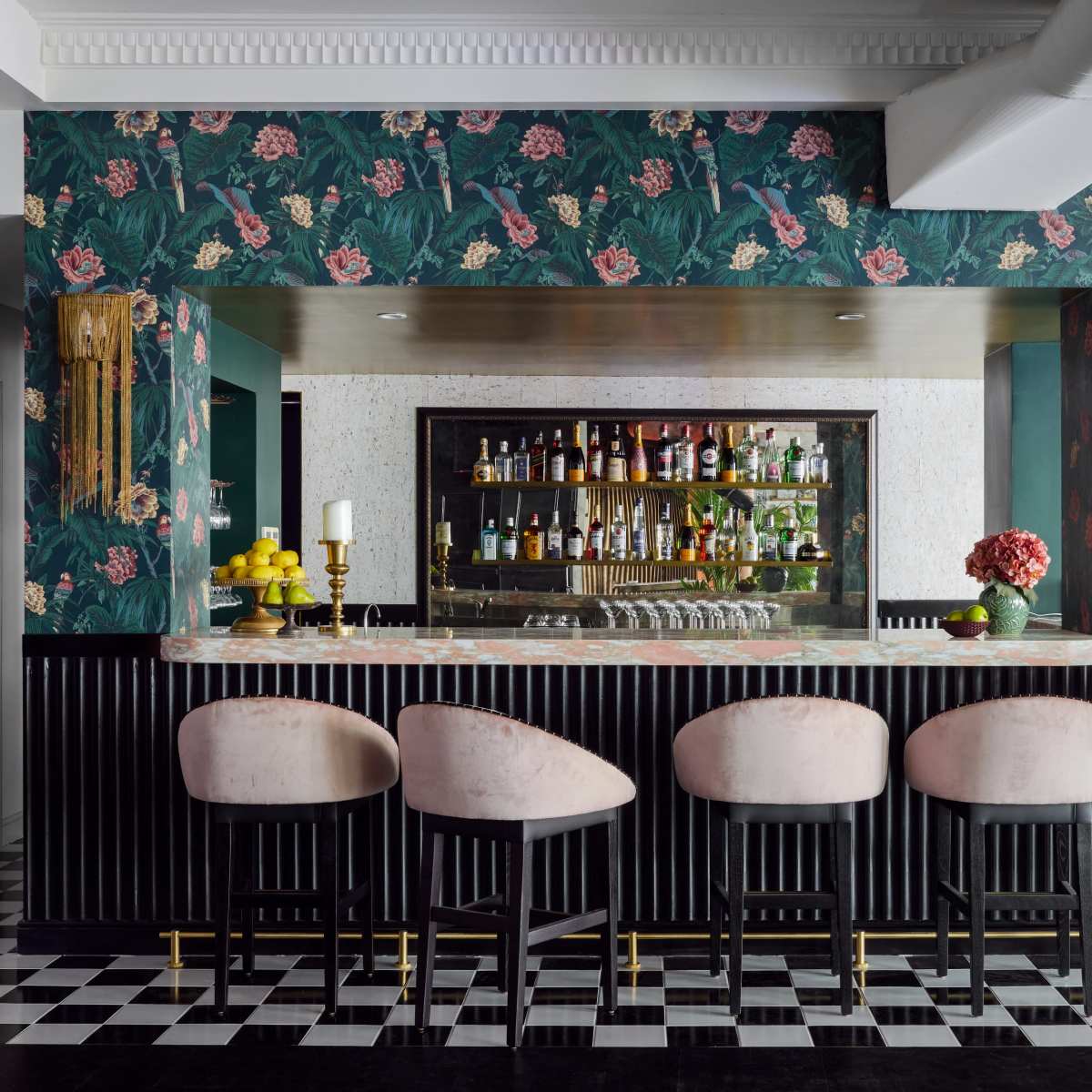 A stylish bar area with a floral wallpaper backdrop, a polished counter, and four upholstered stools in front.