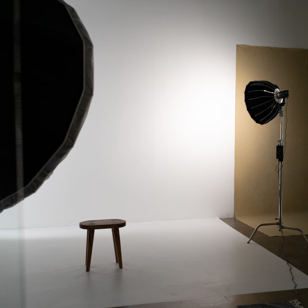 A photography studio setup featuring a wooden stool, a backdrop, and studio lighting equipment.