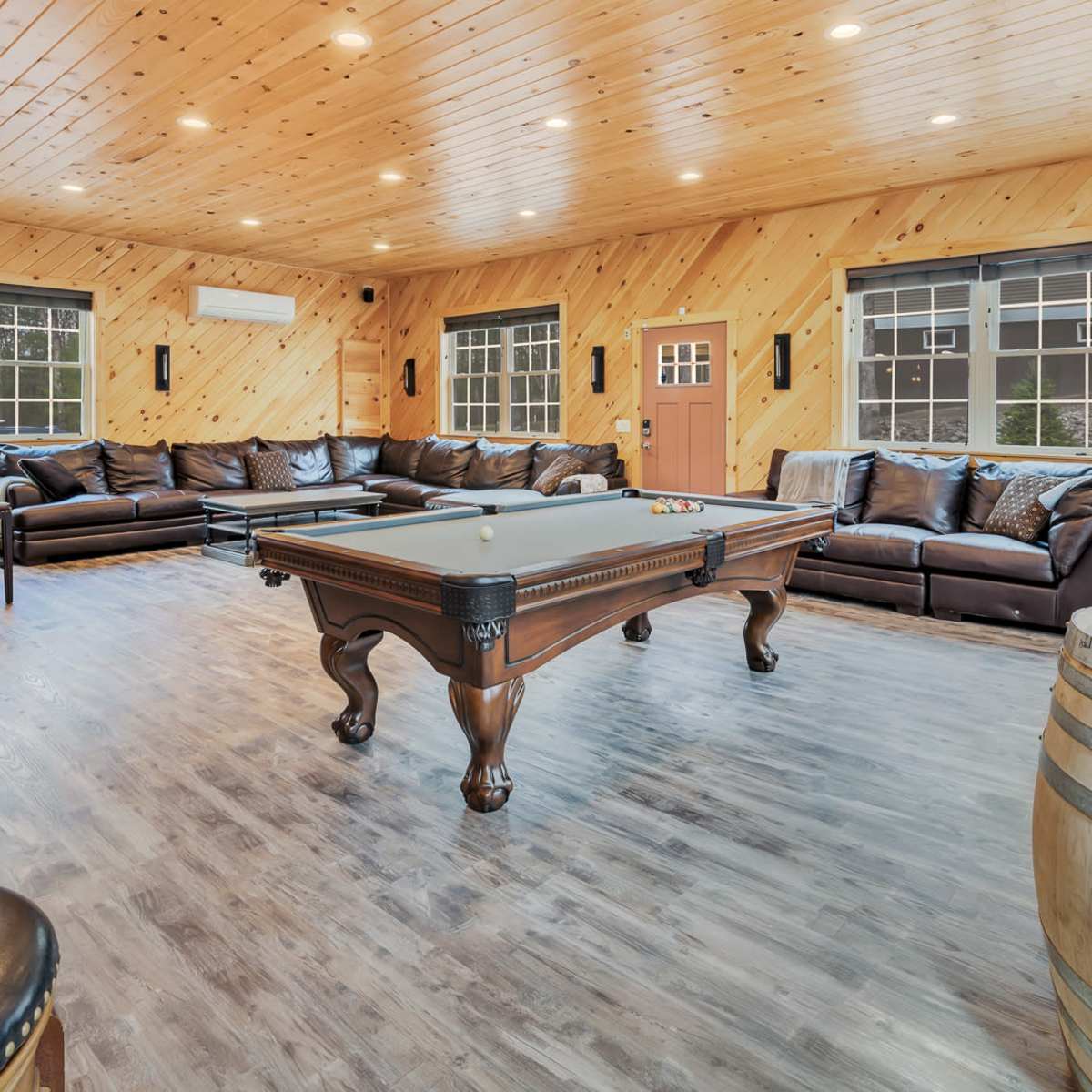 A large game room with a pool table, leather sofas, and wooden accents, illuminated by recessed lighting.
