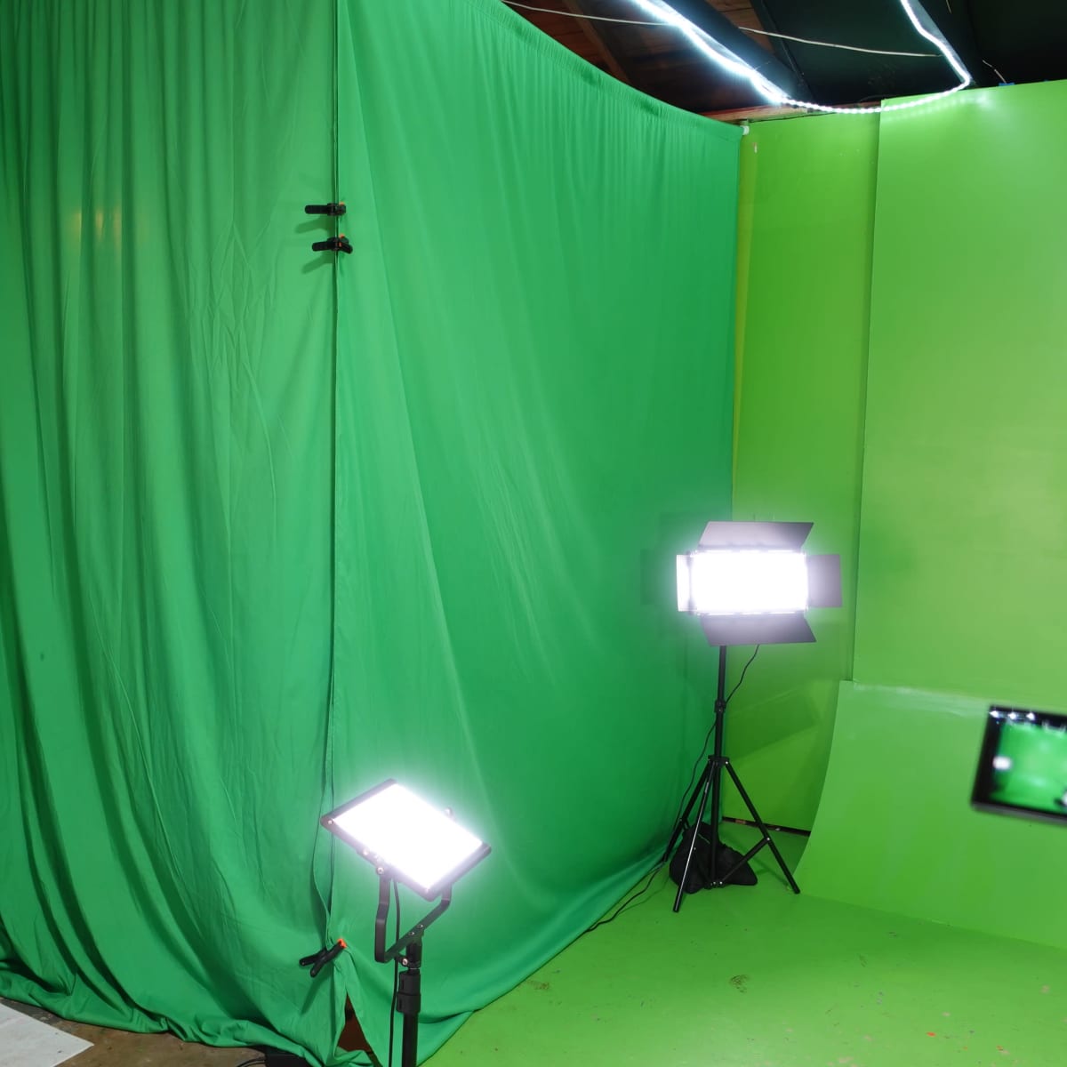 A green screen setup with two bright lights, a camera, and a doorway in a dimly lit room.