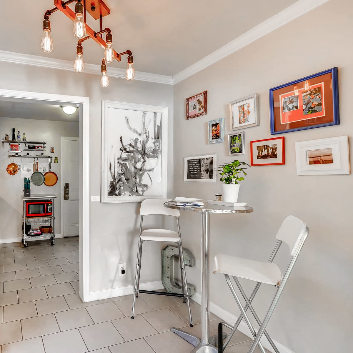 A small dining area with a round table and two white chairs, adjacent to an entryway featuring a red cabinet and various framed pictures on the wall.