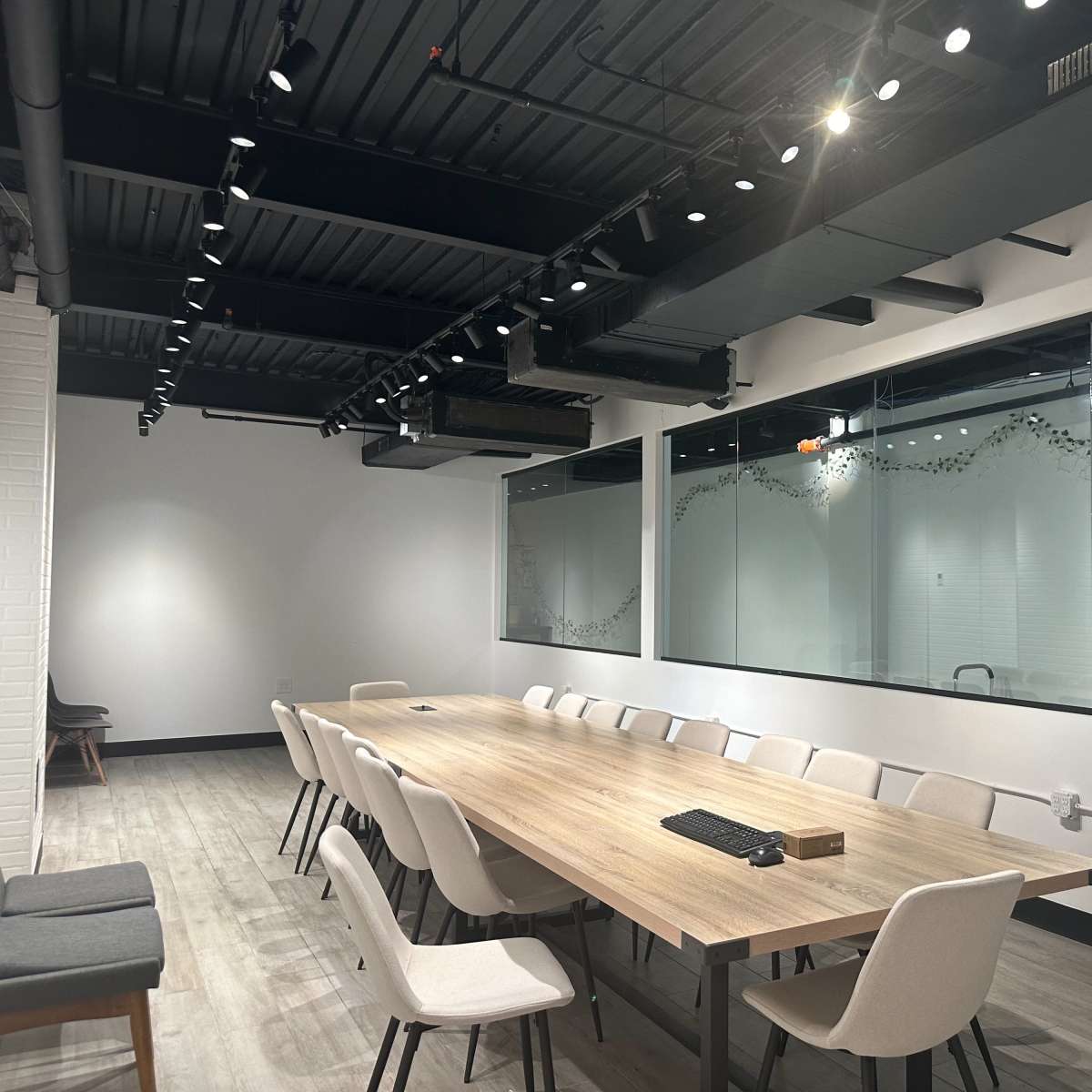 A large, modern conference room features a long wooden table surrounded by white chairs, with glass walls showcasing adjacent meeting spaces.