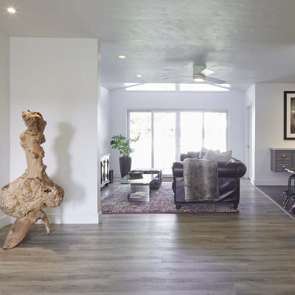 A spacious living area features a combination of modern furniture, a decorative wooden sculpture, and large windows that allow natural light to fill the room.