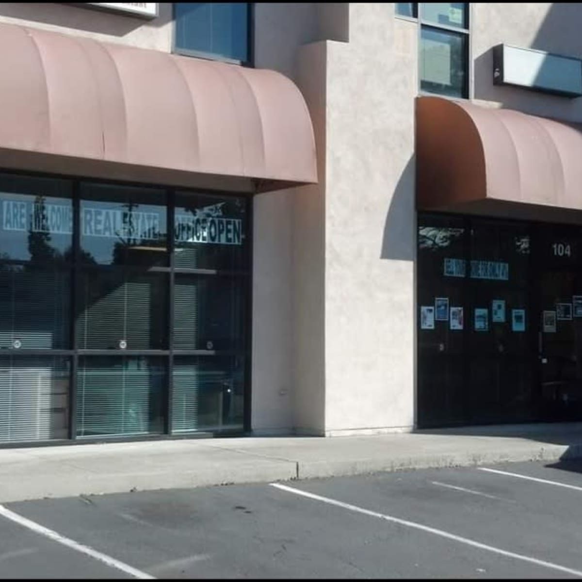 A commercial building with two storefronts, one featuring large windows and a sign indicating that walk-ins are welcome and the business is open.