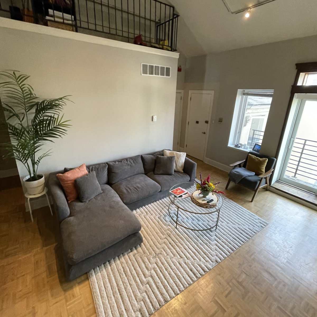 A modern living space features a gray sectional sofa, a round coffee table, and large windows with natural light.