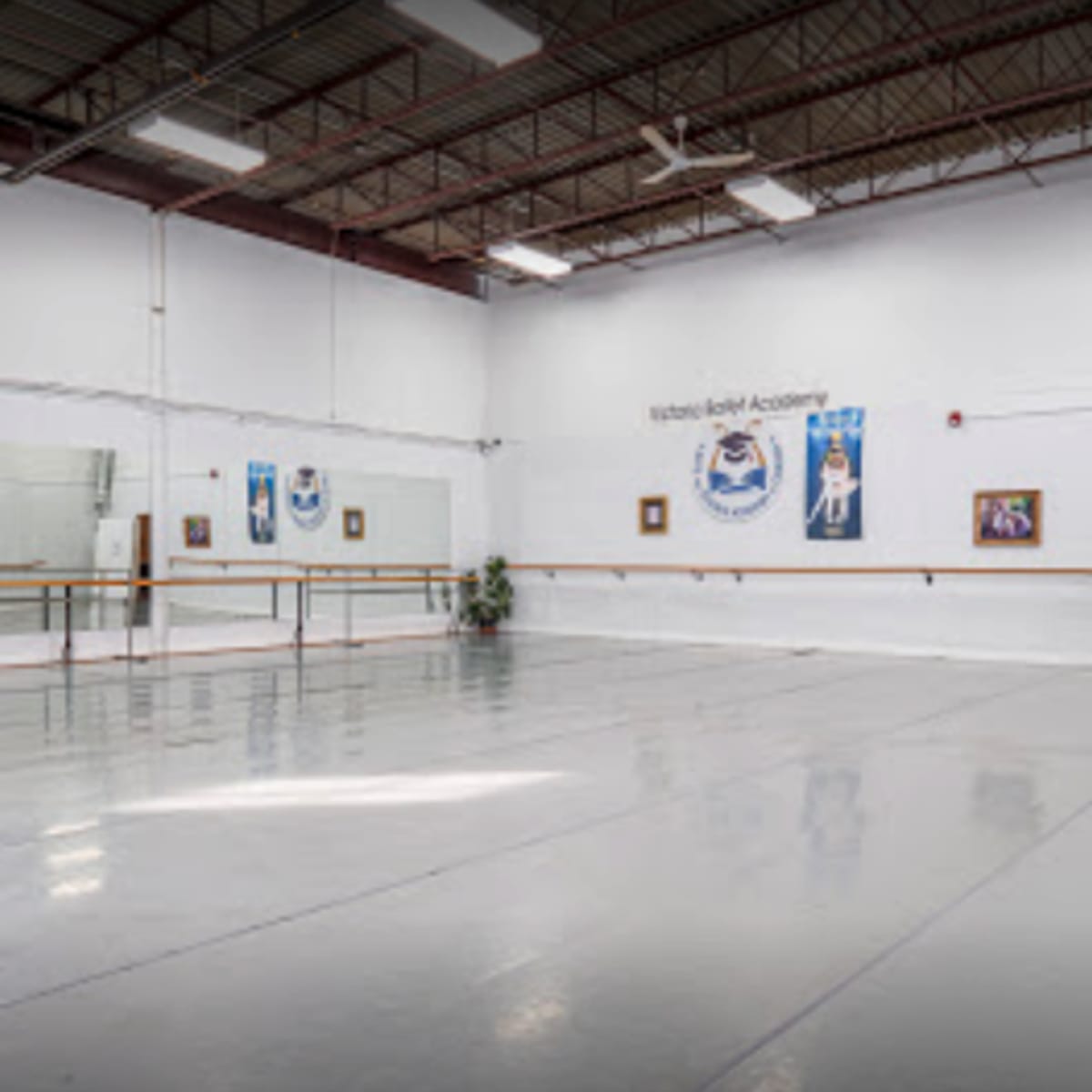 A spacious ballet studio with mirrored walls, ballet barres, and artwork displayed on the white walls.