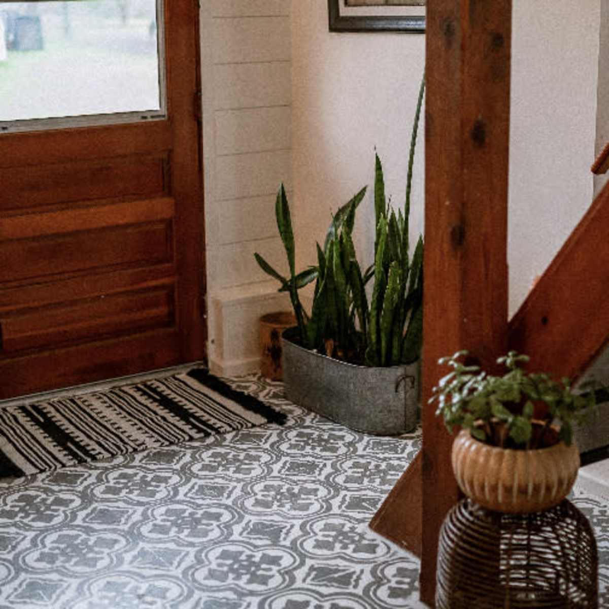 An entryway with a wooden door, a patterned rug, a potted plant in a metal container, and a staircase.