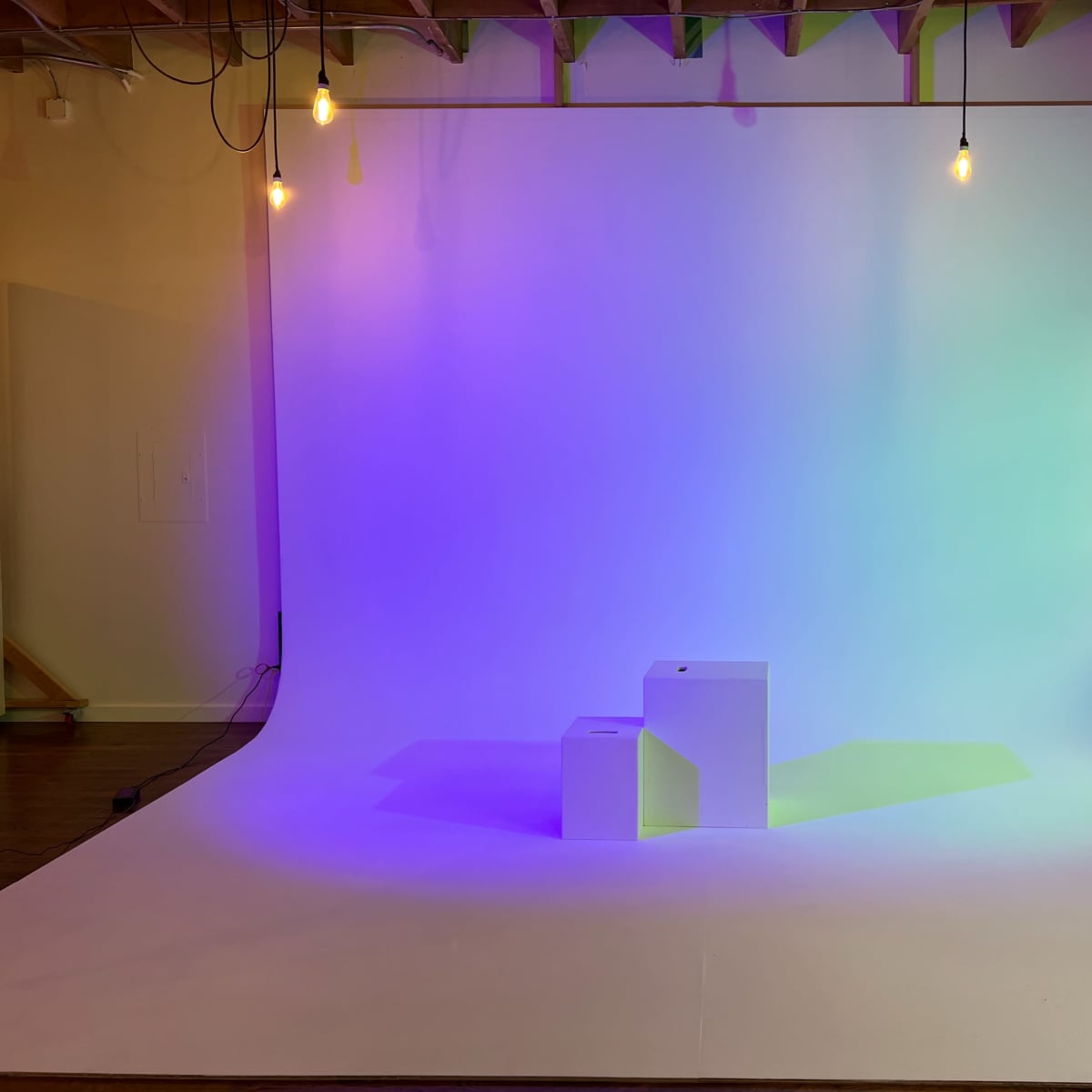A well-lit studio space with a gradient backdrop and two white pedestals positioned in front of it.
