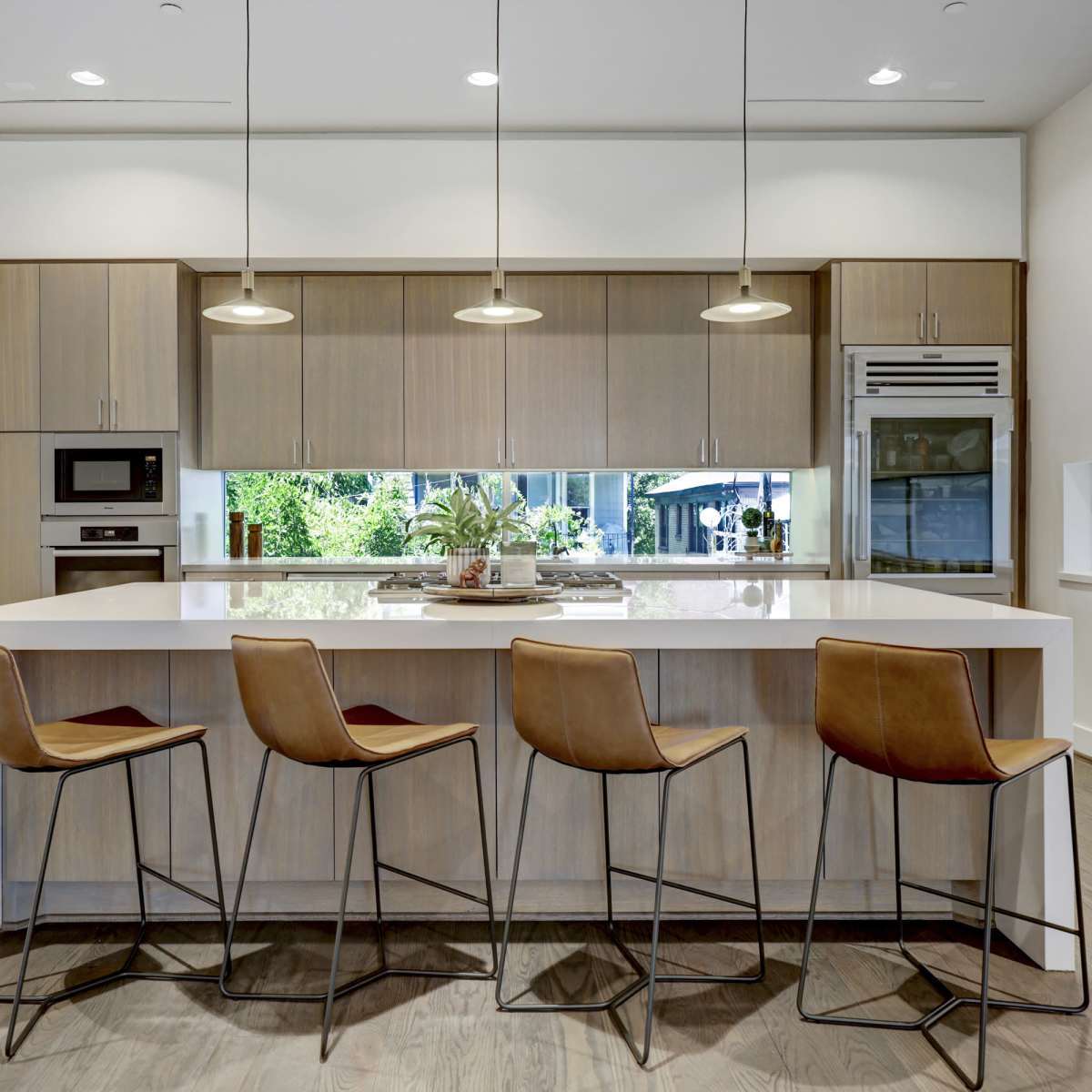 A modern kitchen features a central island with four brown bar stools and stainless steel appliances.