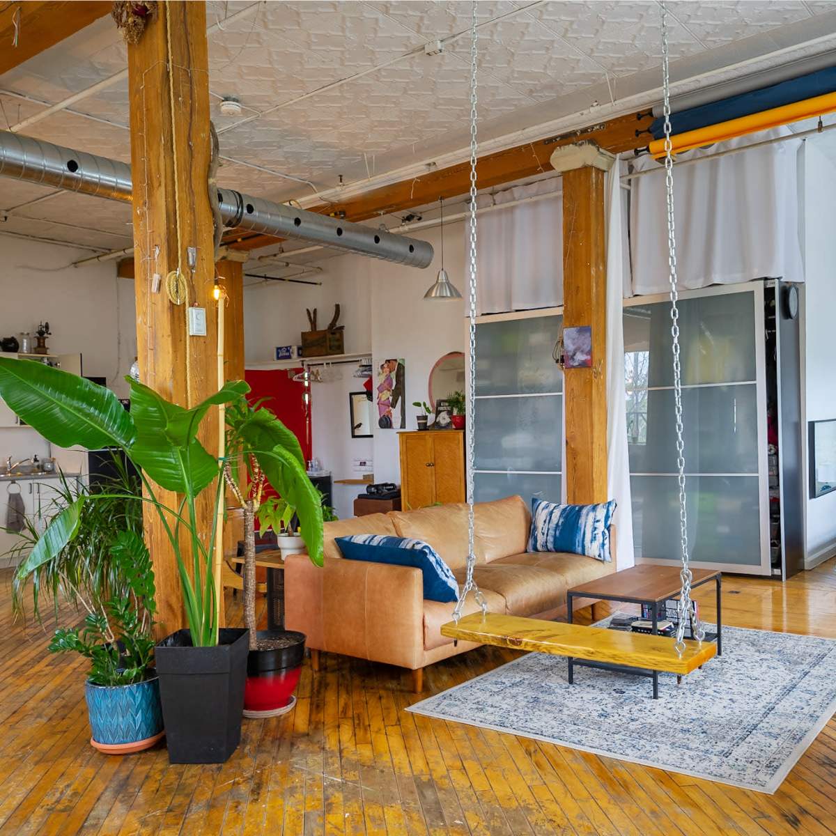A spacious, open living area with wooden floors, featuring a mix of seating options, a large plant, and sliding glass doors.