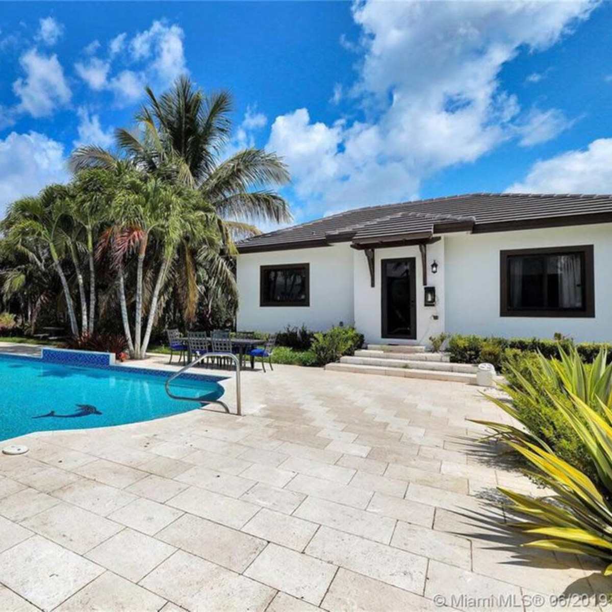 A residential backyard with a swimming pool surrounded by palm trees and a house in the background.