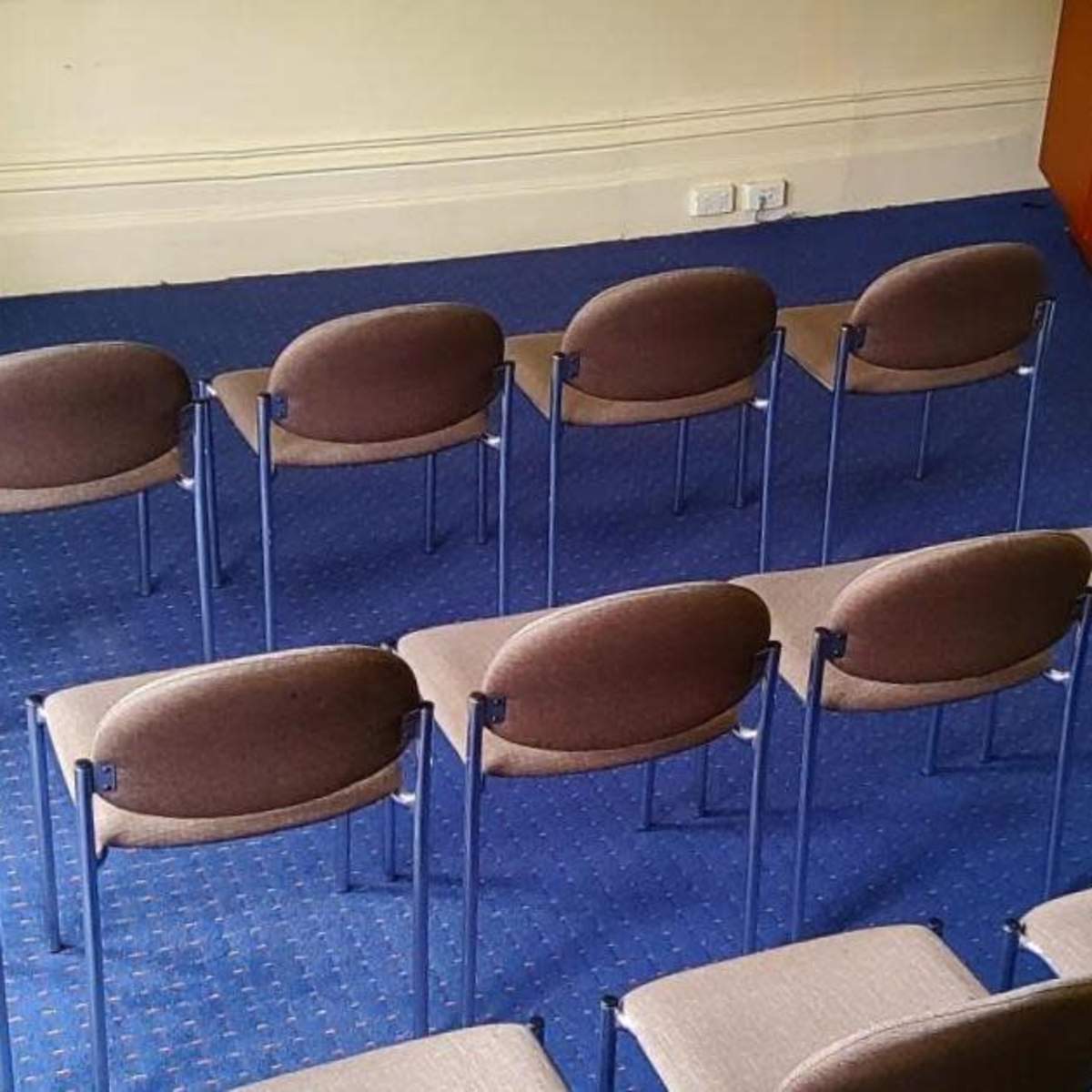 A set of brown chairs is arranged in rows on a blue carpet in a room with a wooden cabinet and a fireplace.