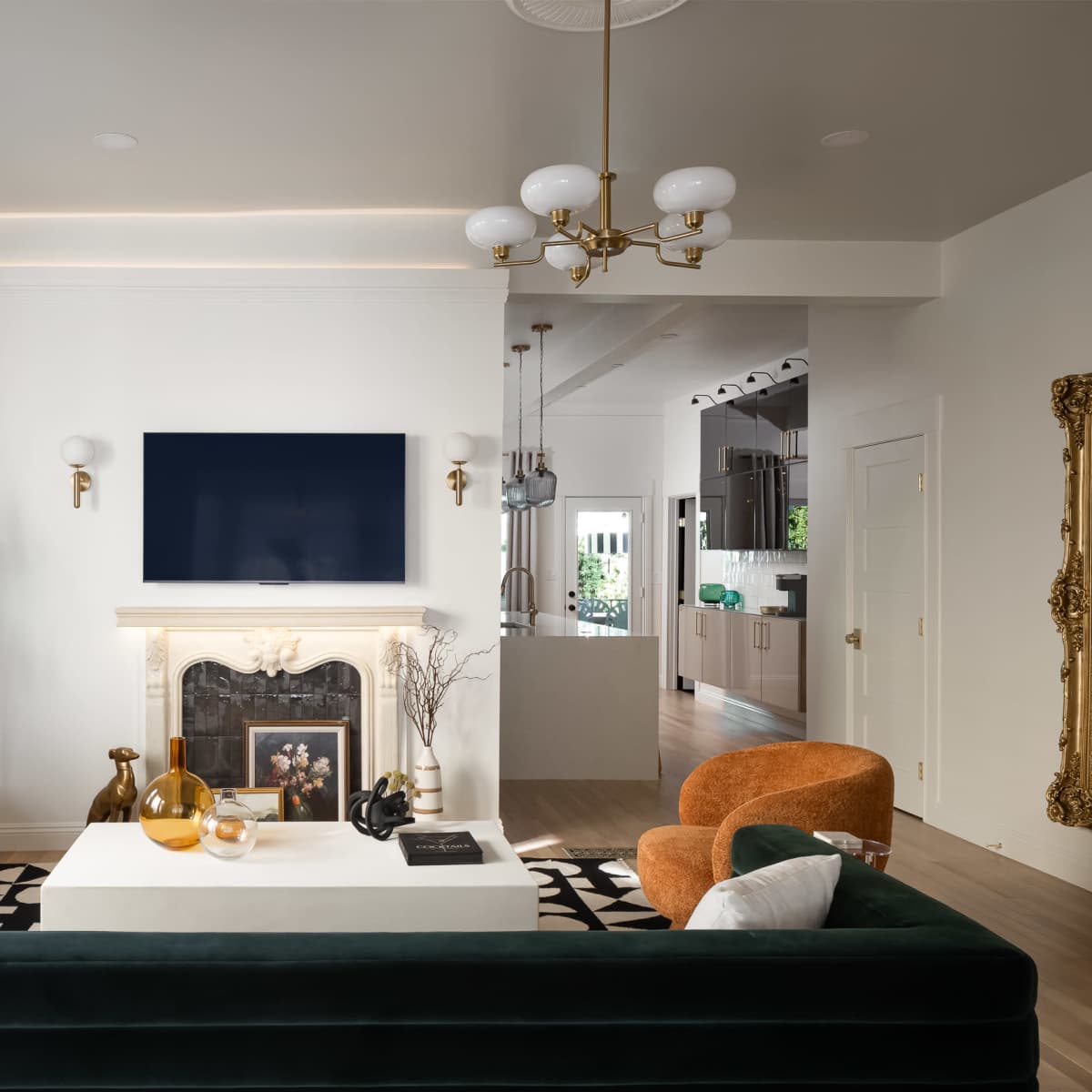 A modern living room features a green sofa, two orange armchairs, a white coffee table, and a wall-mounted plasma TV above a fireplace.